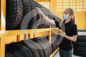Asian female worker wear a mask to prevent the spread of corona virus or COVID-19 checking the stock of car tires at warehouse and photo