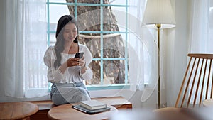 Asian female working at cafe diligently typing and discussing work on smartphone