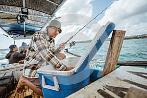 Asian fisherman checking bait in box in small fishing boat