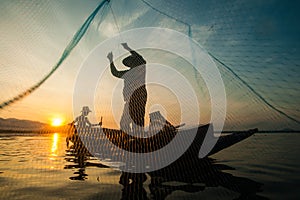 Asian fisherman on wooden boat casting a net for catching freshwater fish