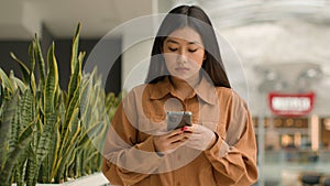 Asian focused woman walking in shopping mall with smartphone look at mobile phone screen Chinese korean girl