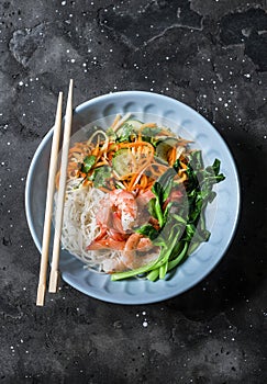 Asian food bowl - rice noodles, shrimp, cabbage bok choy and quickly pickled vegetables carrots, cucumbers, daikon salad on a dark