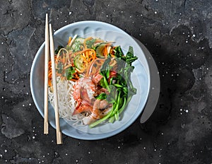 Asian food bowl - rice noodles, shrimp, cabbage bok choy and quickly pickled vegetables carrots, cucumbers, daikon salad on a dark