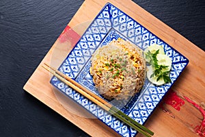 Asian food concept homemade egg fried rice in square ceramic asian style plate on wooden board and black background with copy