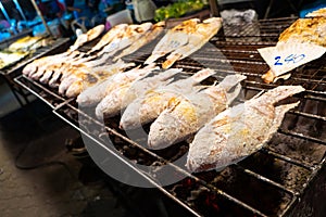 Asian food. Counter with fish in salt on the grill at a night food street market