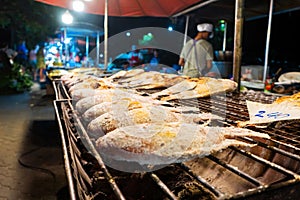 Asian food. Counter with fish in salt on the grill at a night food street market
