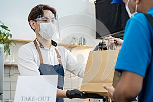 Asian Food delivery man receive beverage order from restaurant worker. Waiter wearing protective mask due to Covid-19 pandemic,