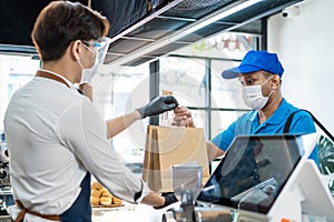 Asian Food delivery man receive beverage order from restaurant worker. Waiter wearing protective mask due to Covid-19 pandemic,