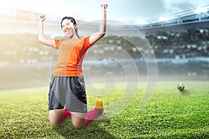 Asian football player woman celebrate her goal with raised arms and kneeling