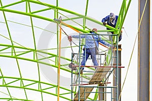 Asian foreman and construction worker on scaffolding are repairing metal roof structure of industrial building