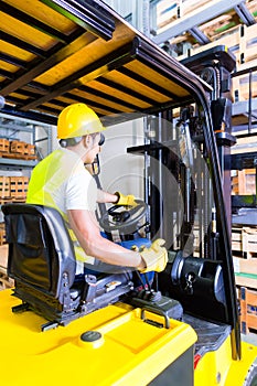 Asian fork lift truck driver lifting pallet in storage