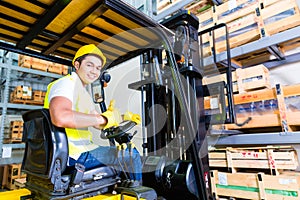 Asian fork lift truck driver lifting pallet in storage photo