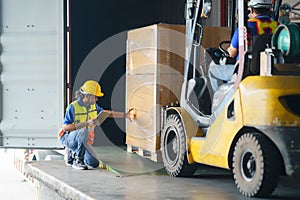 Asian forklift driver loading a shipping cargo container with a full pallet with boxes in logistics port terminal. Asian warehouse