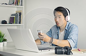 Asian Freelance Videographer Work from Home Checking Multimedia File by Smartphone and Laptop in Home Office