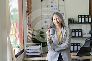 Asian freelance woman casually holding coffee mug working with tablet for internet surfing