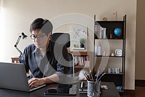 Asian freelancer business man working at home using laptop computer at workspace office desk in living room. Remote work from home