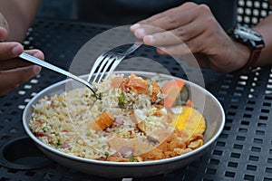 Asian fried rice with vegetables and sunny side egg scooped with spoon and fork with blurred background.