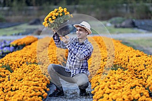 Asian gardener is inspecting the health and pest control of orange marigold pot while working in his rural field farm for