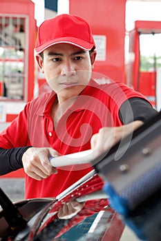 Asian gas station worker in red uniform cleaning the car windshield with window squeegee