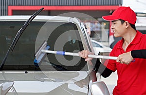 Asian gas station worker in red uniform cleaning the car windshield with window squeegee