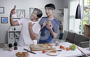 Asian gay couple looking happy while cooking and taking selfie. LGBT men couple preparing meal salad in the kitchen at home