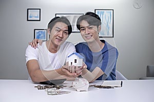 Asian gay couple saving money to buy a house, looking at camera. LGBT male couple saving money for family and home