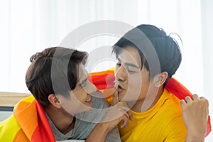 Asian gay homosexual couple playful and romantic moment on the bed. While trying to kiss to each other. With rainbow flag as LGBT