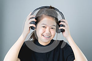 Asian girl in black casual dress listening to music from black headphones. In a comfortable and good mood.