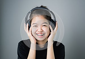 Asian girl in black casual dress listening to music from black headphones. In a comfortable and good mood.