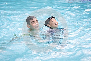 Asian girl and boy playing water and swimming together in the swimming pool with fun.