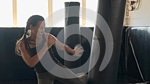 Asian girl brunette fighter punches and kicks on a black punching bag. Sports, kickboxing, boxing, gym