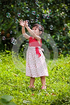 Asian girl catches soap bubbles on nature background. Outdoors.