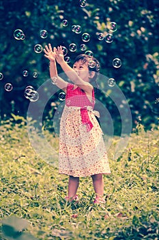 Asian girl catches soap bubbles on nature background. Outdoors.