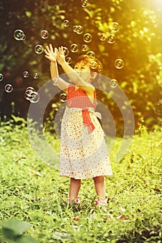 Asian girl catches soap bubbles on nature background. Outdoors.
