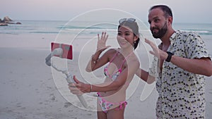 Asian girl and caucasian man greeting live stream viewers during broadcast video filming at tropical beach. Woman