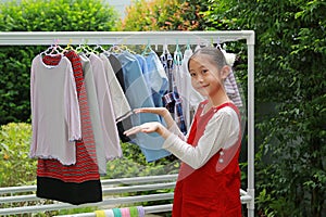 Asian girl child helping to do dry the clothes at the garden near house. Kid hanging cloth on a clothesline