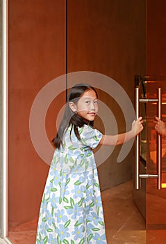 Asian girl child opens the big glass door of a cozy cafe