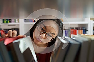 Asian girl choosing book while in bookstore, female student searching for primary sources in library