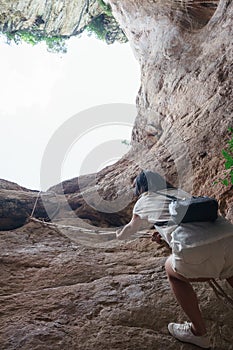 Asian girl climbing up rope on rocky cliff