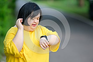 Asian girl with Down syndrome watch fitness watch happy smile By walking to burn fat and jogging slowly to exercise in a park in