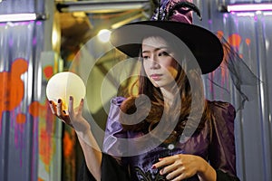 Asian girl dressed as a witch holding a magic crystal ball in hand and casting a spell