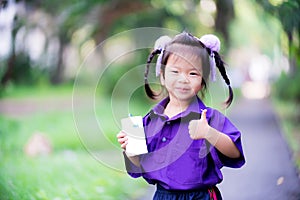Asian girl drink milk. Child holds white milk box  a blue tube in her hand. Cute children to raise the thumb for admire or support