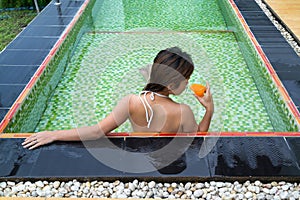 Asian girl drinking glass of orange juice in the pool