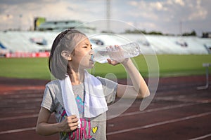 Asian girl drinking water from plastic bottles after jogging, little girl drink thirsty water due to hot weather after run in the