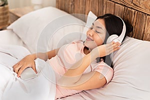 Asian Girl In Earphones Listening Music In Bed At Home