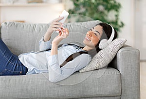 Asian girl enjoying listening music on smartphone with wireless headphones at home