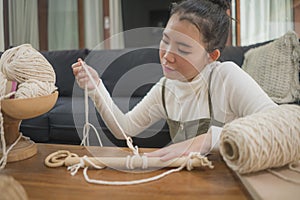 Asian girl enjoying macrame handcraft hobby - young happy and pretty Korean woman at home doing macramÃ© using ropes and cords and