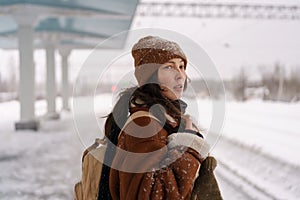 Asian girl going on winter journey feel cold waiting for train arrival outdoors at snowy station