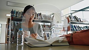 Asian girl with hand on head feeling tired and stressed while read books and take medicine in library at university