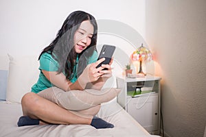 Asian girl with hand phone - home lifestyle portrait of young happy and attractive Korean woman on bed using internet mobile